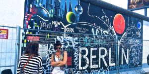 man wearing black waistcoat and white tank tops standing near a mural